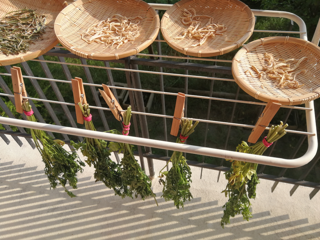 less waste z pietruszką - na balkonowej suszarce rozwieszone bukieciki suszącej się naci, na bambusowych plecionych koszyczkach suszące się w słońcu łodyżki i korzenie pietruszki posiekane w słupki
