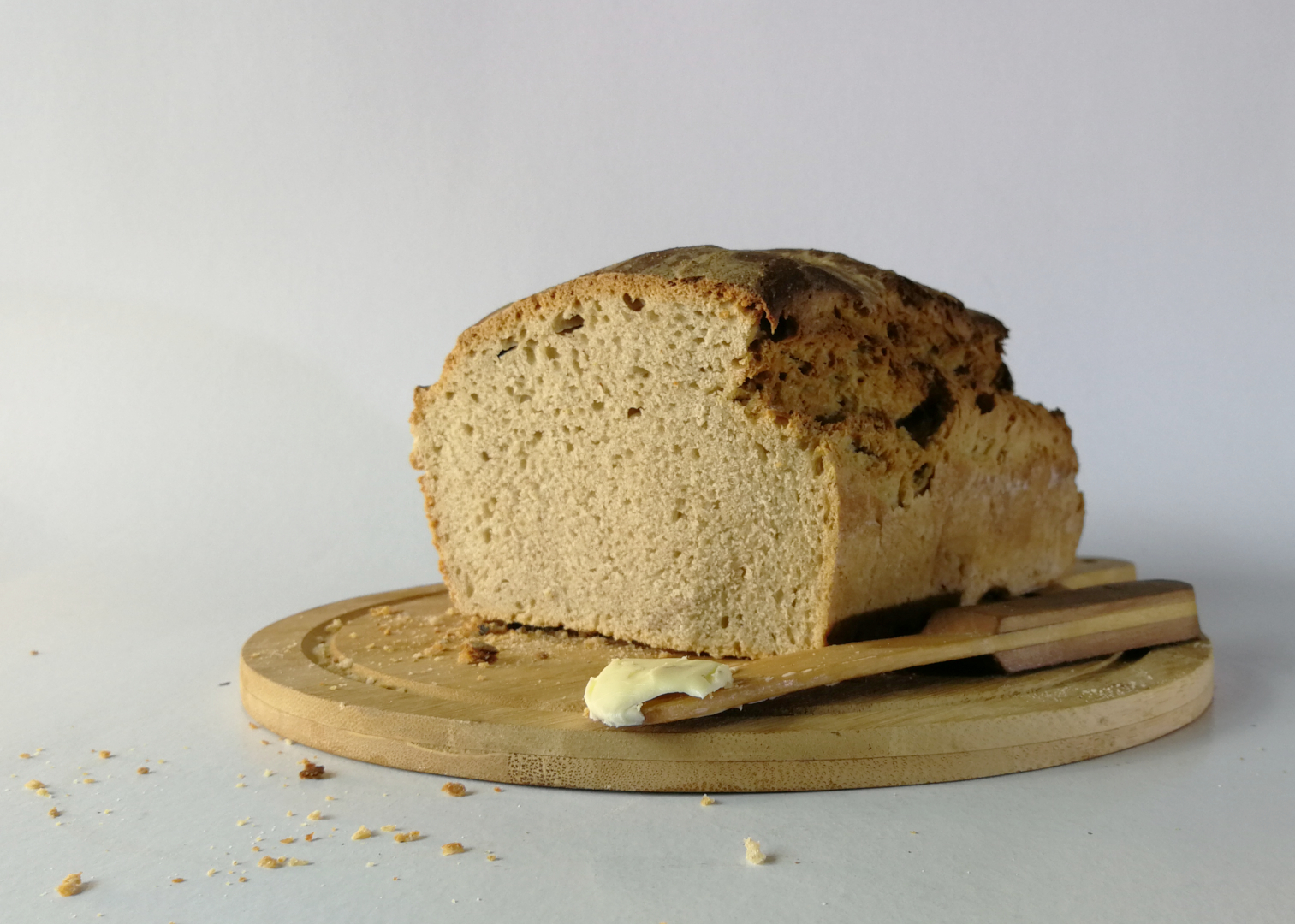 kalkulacja pieczenia chleba w domu, chleb tostosy na desce obok drewniany nóż z odrobiną masła