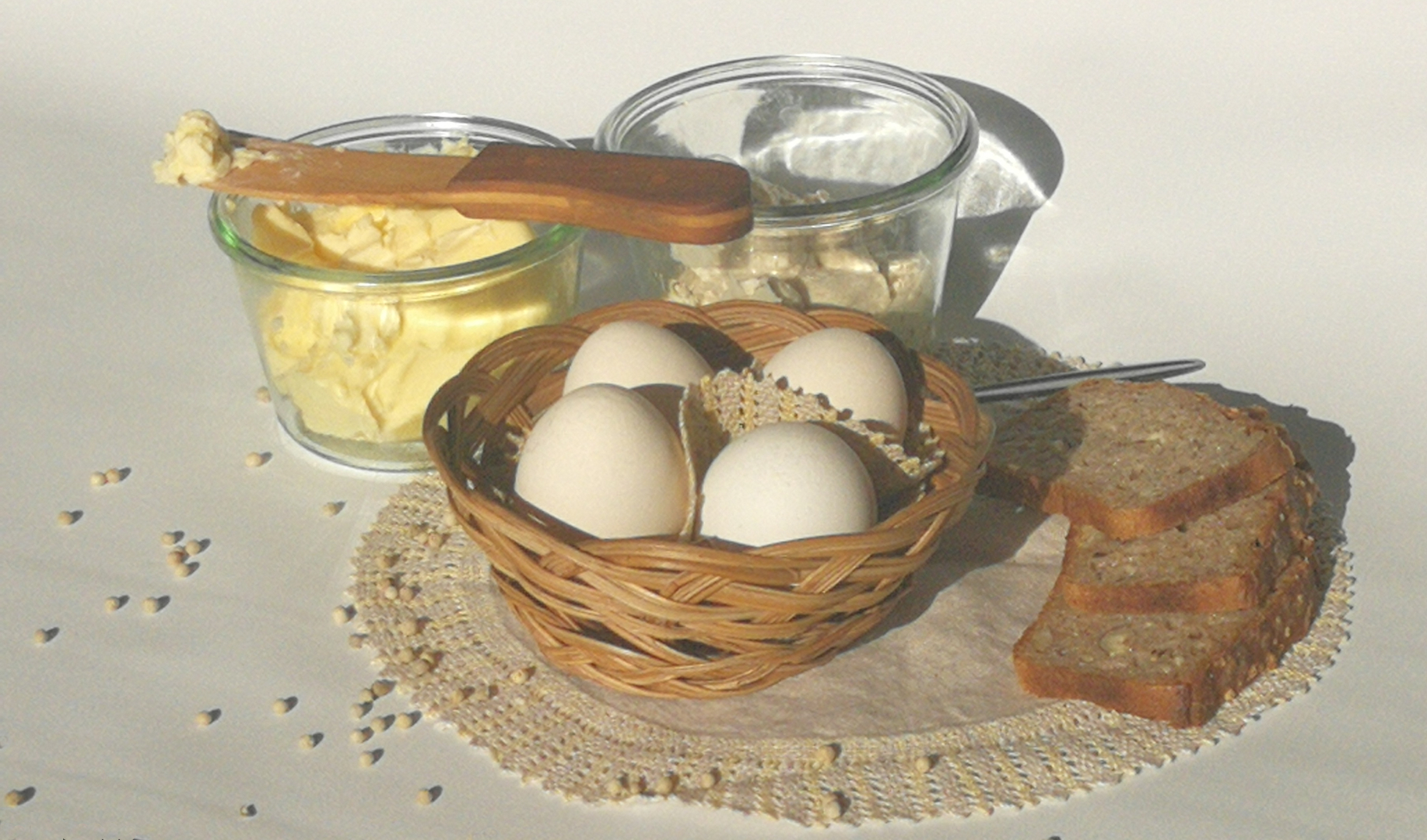 jajka w koszyku, obok masło i twarożek w szklanych słoikach, kromki chleba