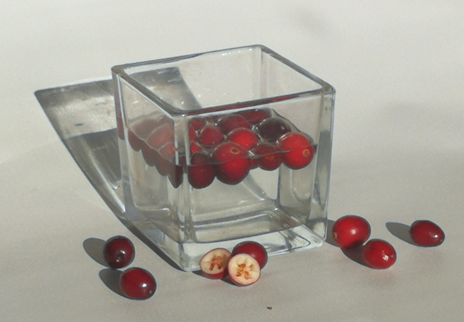 owoce żurawiny unoszące się na wodzie w szklanym pojemniku, obok rozrzycowne owoce, jeden przekrojony