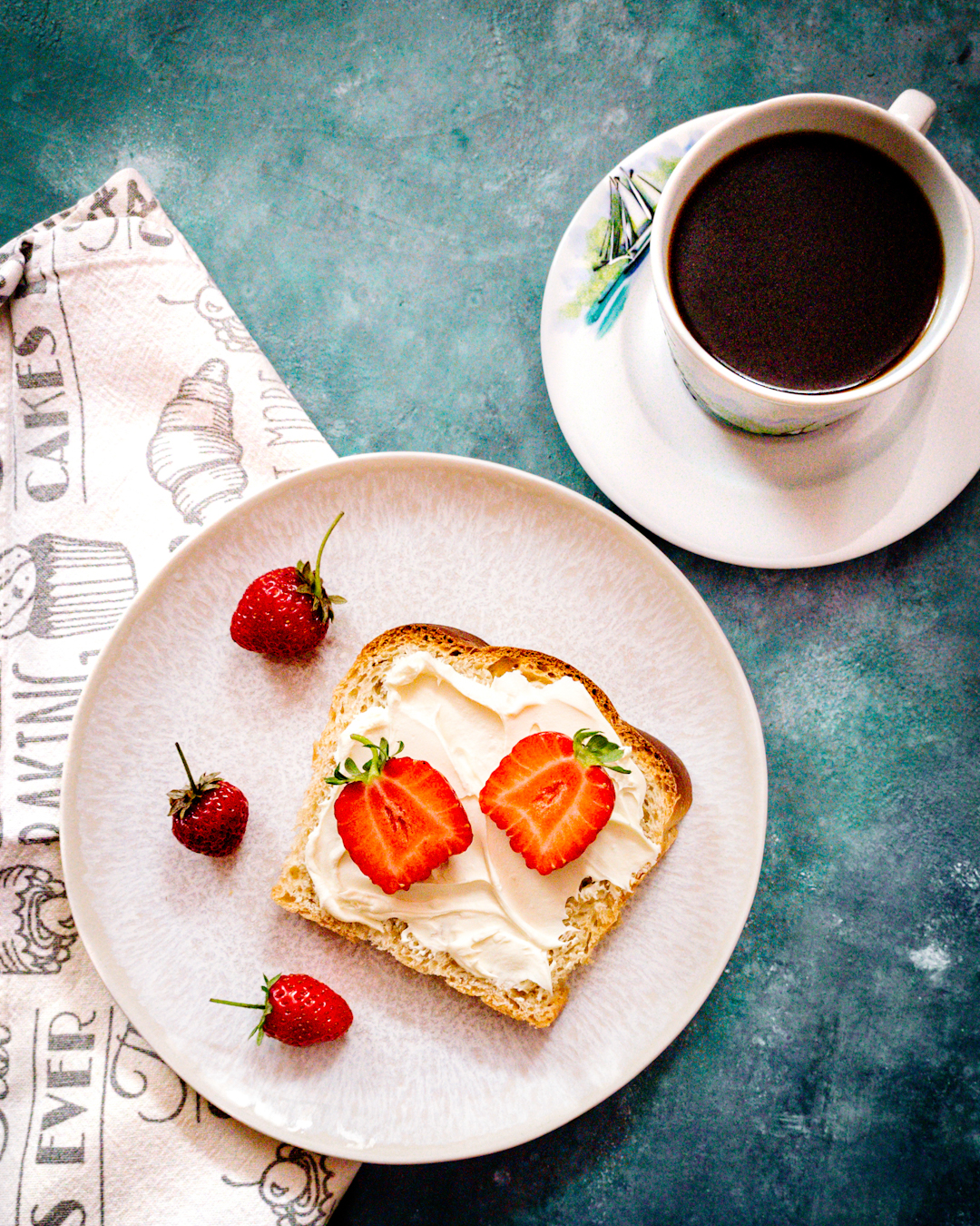 śniadanie - kromka chałki z serkiem mascarpone i truskawkami, obok kawa