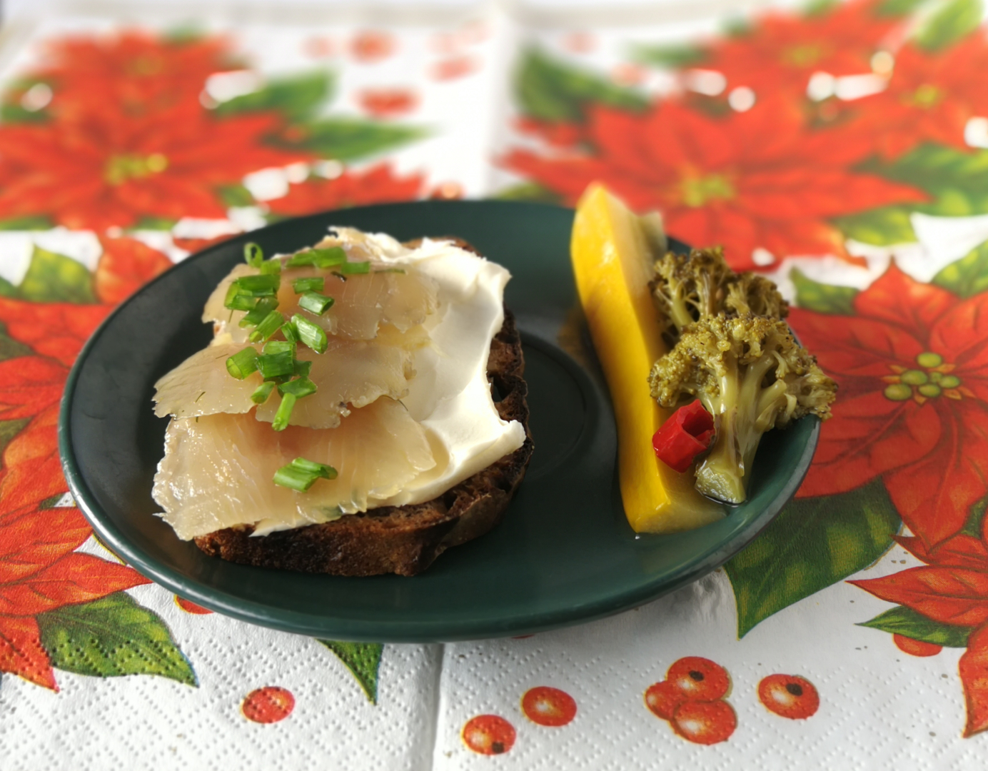 kanapka z ciemnego pieczywa z białym serem i gravlaxem posypana szczypiorkiem, obok na talerzyku pikle z warzyw