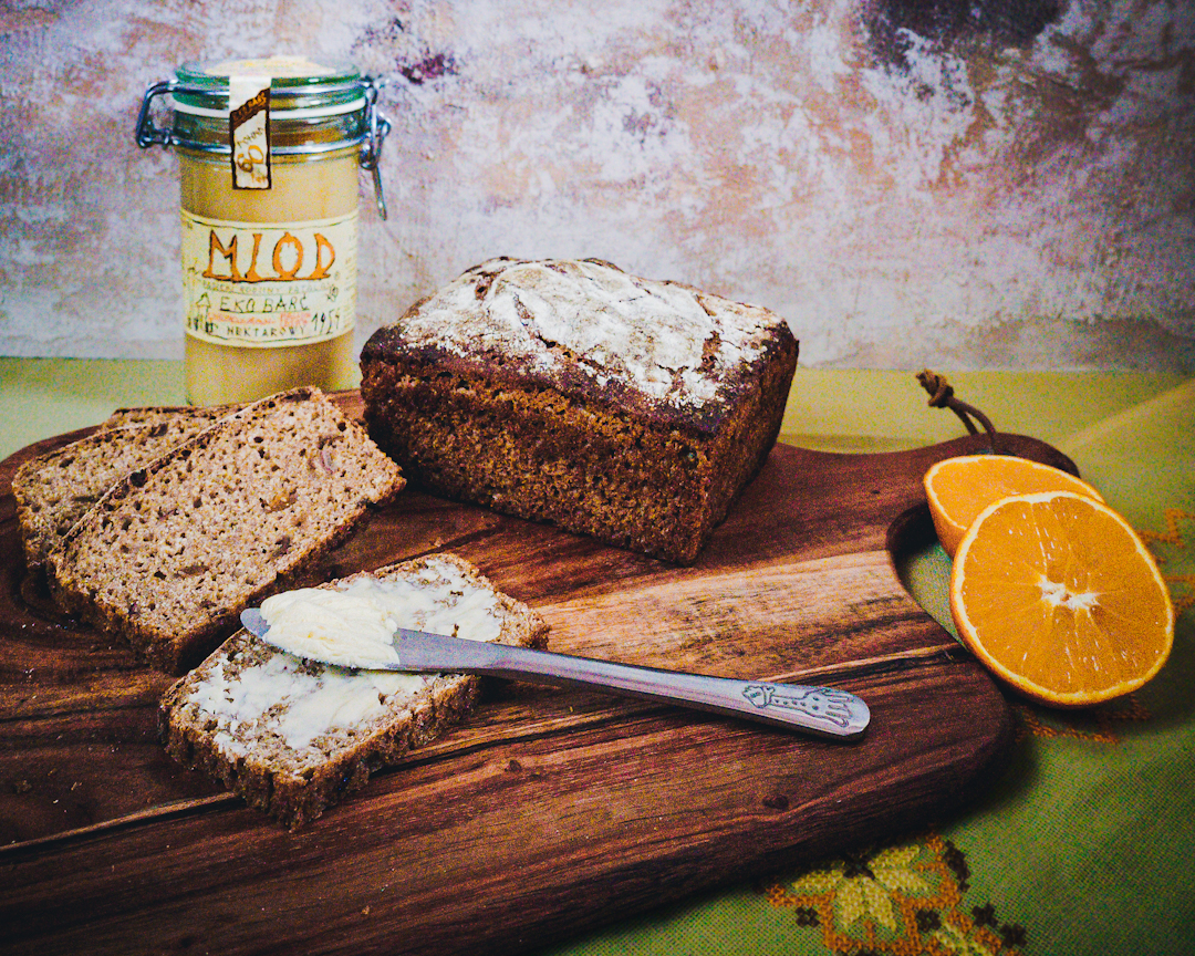 kromki chlebka bakaliowego z masłem, cały bochenek i dodatki: miód i pomarańcze