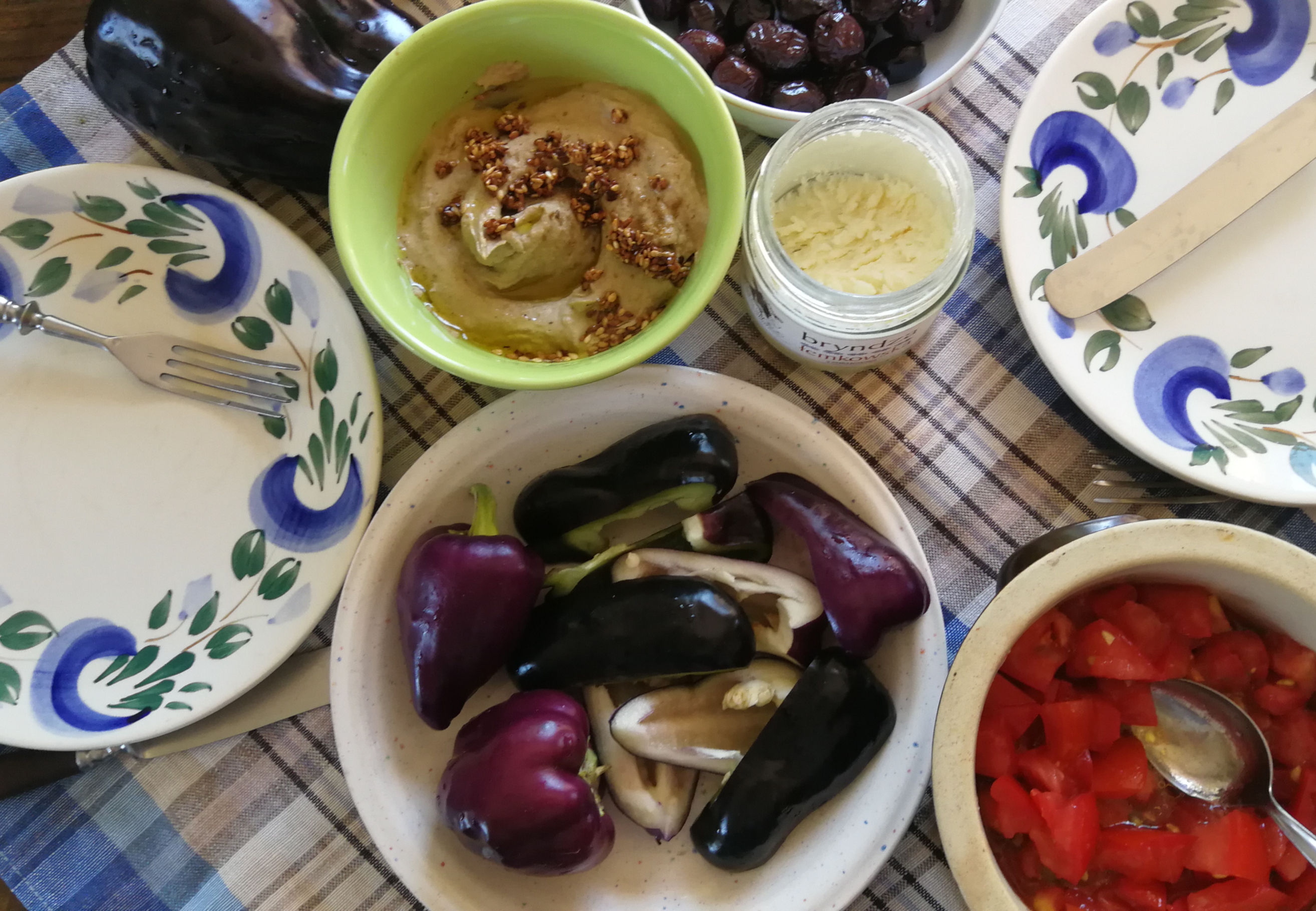baba ganoush, czarne oliwki, czarna i fioletowa papryka, sałatka z pomidorów, bryndza na stole nakrytym do śniadania